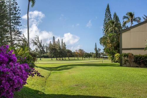 a green yard with trees and a building and purple flowers at Fantastic Location on the golf course near the beach in Kahuku