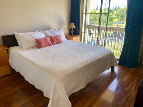a bedroom with a white bed with two pillows and a window at Relaxing Turtle Bay townhome near the beach in Kahuku