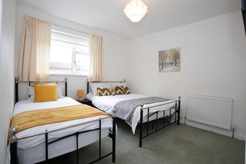 two beds in a room with white walls and a window at Hurley House in Cheadle Hulme