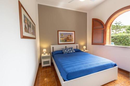 een slaapkamer met een bed met blauwe lakens en een raam bij 3-Casa sul mare con piscina vicino Cefalù in Campofelice di Roccella