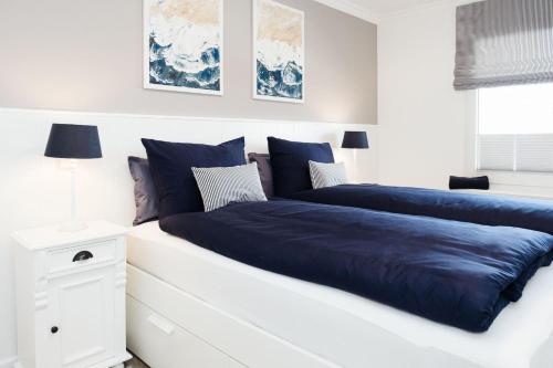1 dormitorio blanco con 2 camas y sábanas azules en Norderhoog-Whg-35-1-OG-Wohnung-35, en Westerland