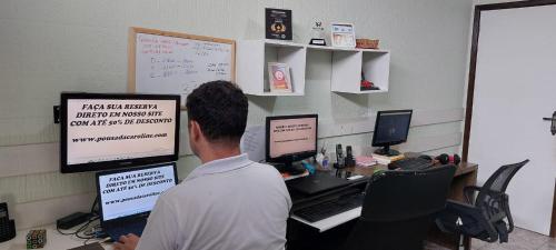 a man sitting at a desk with two computers at Hotel e Pousada Caroline in Foz do Iguaçu