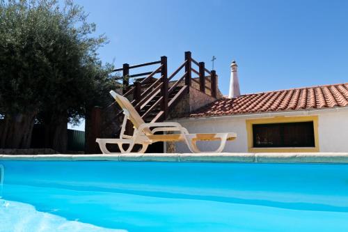 a swimming pool with two chairs and a house at B&B Quinta da Romãzeira in São Bartolomeu de Messines