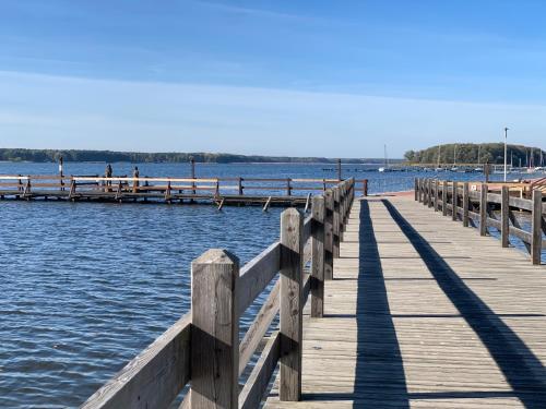 a wooden pier with people sitting on benches on the water at Przy Złotych Piaskach 1 in Sława