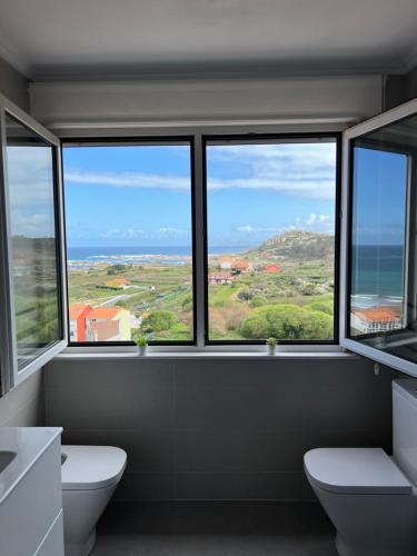 Apartamentos Maria de Lucia- Ático في Arou: حمام بثلاث نوافذ مطل على المحيط