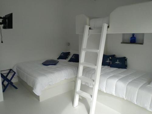 a white bedroom with two beds and a ladder at Νissos K in Mérikhas