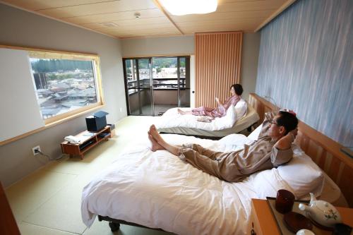 two people laying on beds in a hotel room at Honjin Hiranoya Annex in Takayama