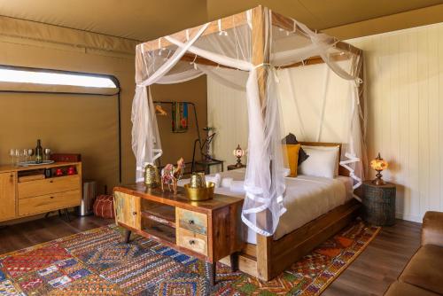 a bedroom with a canopy bed with a wooden table at Two Fat Blokes Moroccan Glamping in Pokolbin