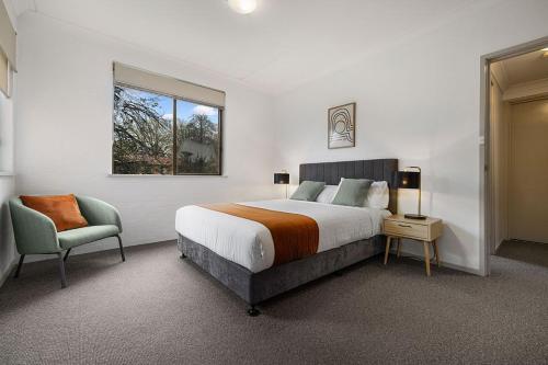 een slaapkamer met een bed, een stoel en een raam bij Oxley Court Serviced Apartments in Canberra