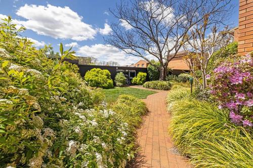 a brick path through a garden with flowers at Oxley Court Serviced Apartments in Canberra