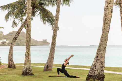 a woman doing yoga on the beach with palm trees at Crowne Plaza Resort Guam in Tumon