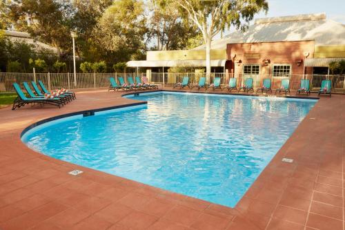 a large swimming pool with chairs and a building at Outback Hotel in Ayers Rock