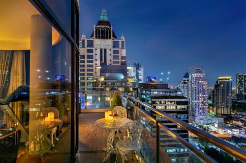 Un balcón con mesas y sillas y un perfil urbano en Bandara Silom Suites, Bangkok en Bangkok