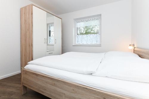 1 dormitorio con 1 cama blanca grande y cabecero de madera en Ferienwohnungen im Haus Deichnest, en Bensersiel