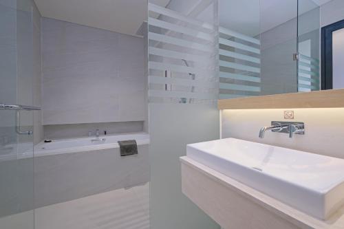 un bagno bianco con lavandino e vasca di Quest Hotel Prime Pemuda - Semarang a Semarang