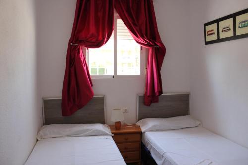 two beds in a room with a window with red curtains at Delfines II Solo Familias Serviplaya in Playa de Xeraco