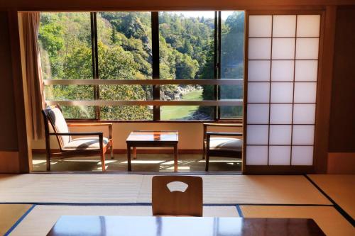 a room with a large window and a table and chairs at 秘境のおやど 龍峡亭　HIKYOUNOOYADO RYUKYOUTEI in Tokimata