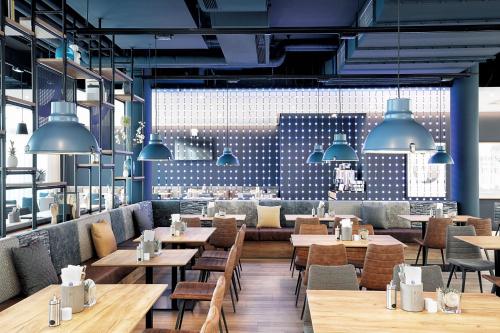 a restaurant with wooden tables and chairs and large windows at H2 Hotel München Olympiapark in Munich