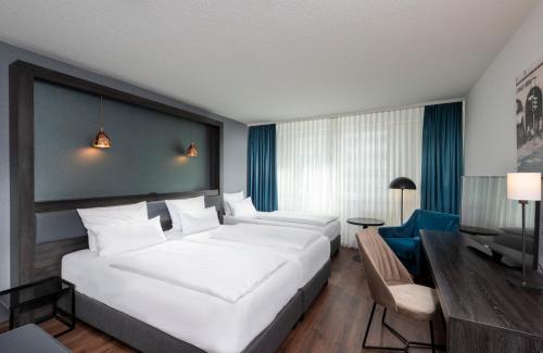 ein Hotelzimmer mit einem großen weißen Bett und einem Schreibtisch in der Unterkunft City Hotel Berlin East in Berlin