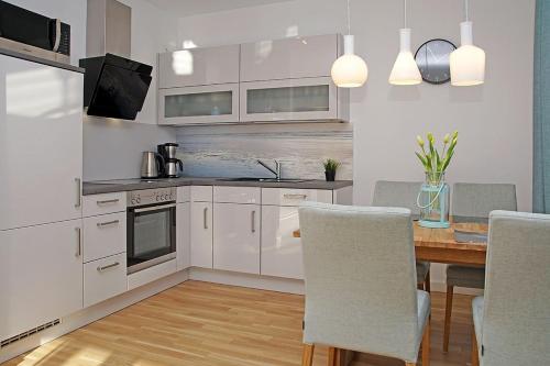 a kitchen with white cabinets and a wooden table with chairs at Haus Yachthafen 4 in Cuxhaven