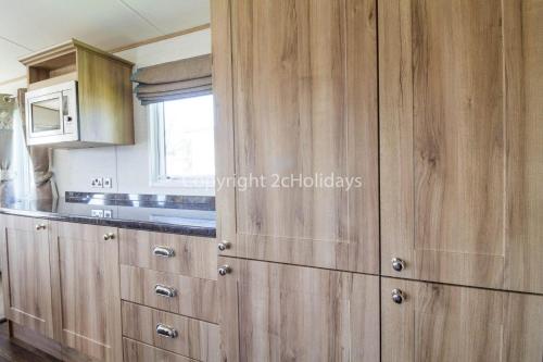 a kitchen with wooden cabinets and a microwave at Brilliant Caravan For Hire At Caister Haven Holiday Park In Norfolk Ref 30011h in Great Yarmouth