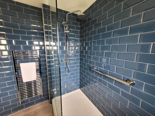 a blue tiled bathroom with a shower with a glass door at Jersey Cottage in Horseheath