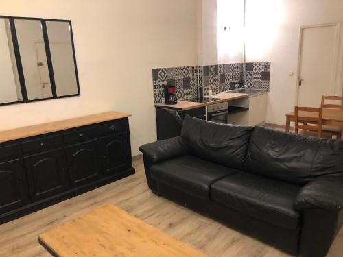 a living room with a black leather couch and a kitchen at Appartement et son jardin à lille fac de droit in Lille
