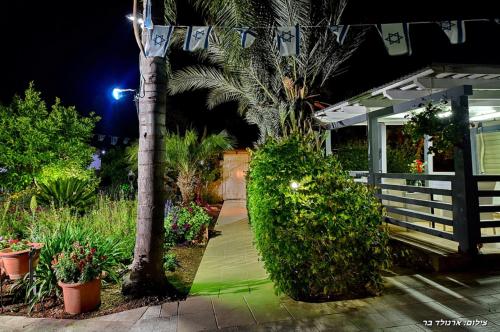 a garden at night with a palm tree and a house at אחוזת אלכסנדר in Elifelet