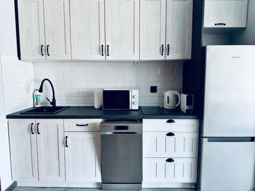 une cuisine avec des armoires blanches, un évier et un réfrigérateur dans l'établissement AL-DOM Apartamenty Apartament 103, à Kołobrzeg