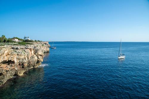 a sail boat in the water next to a cliff at Pierre & Vacances Menorca Cala Blanes in Cala en Blanes