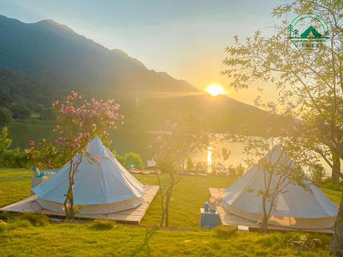 two tents in a field with the sunset in the background at Đào Hoa Glamping in Hanoi