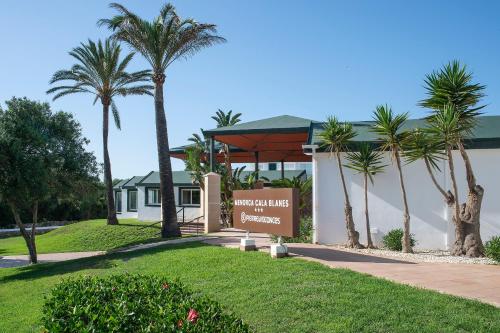 a sign in front of a building with palm trees at Pierre & Vacances Menorca Cala Blanes in Cala en Blanes