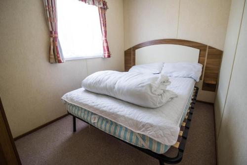 Un pequeño dormitorio con una cama con sábanas blancas y una ventana en 8 Berth Spacious Caravan By The Beach In Norfolk Ref 50059g en Great Yarmouth