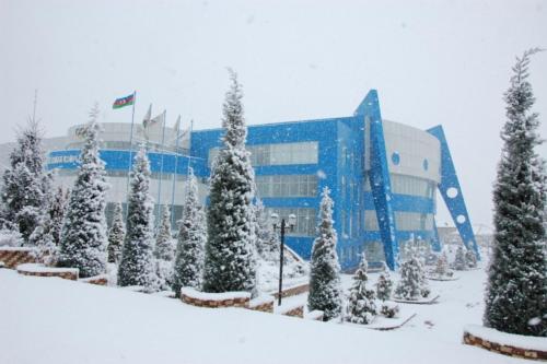 a building covered in snow with trees in front of it at Arena Hotel Gusar in Qusar