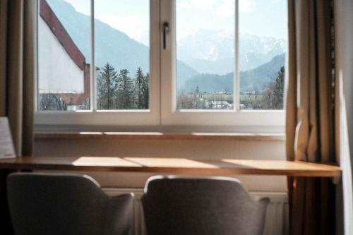 a table with chairs in front of a window with mountains at The Townhouse Ruhpolding - Individual Design & Casual Concept in Ruhpolding