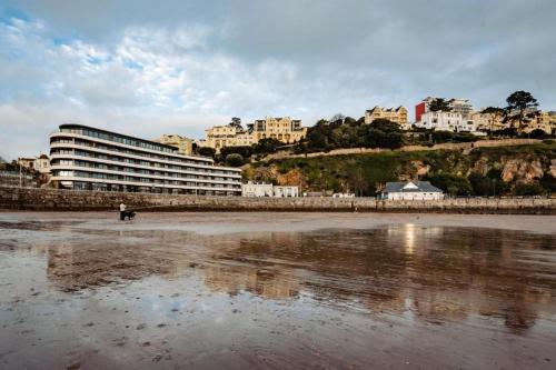 a person walking a dog on the beach with buildings at Sandybanks Torquay - Seaview and Promenade Apartments in Torquay