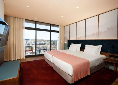 a bedroom with a large bed and a large window at Montebelo Viseu Congress Hotel & Spa in Viseu