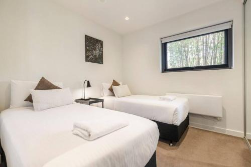 two beds in a white room with a window at Peaceful 2 bedroom unit with Free parking in Melbourne