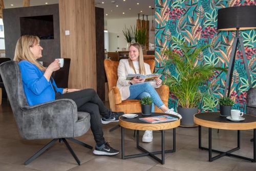 Dos mujeres sentadas en sillas en una habitación con plantas en Alb Inn - Hotel & Apartments, en Merklingen