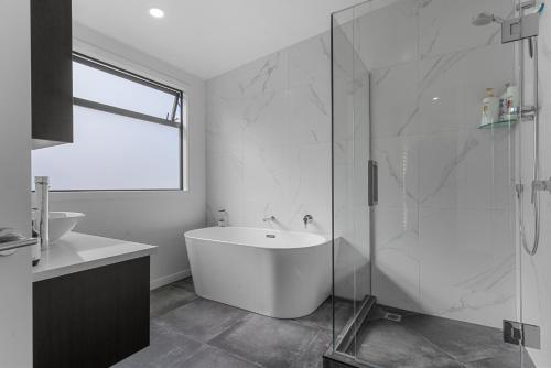 La salle de bains blanche est pourvue d'une baignoire et d'une douche en verre. dans l'établissement Fuel for the Sol - Mangawhai Heads Holiday Home, à Mangawhai