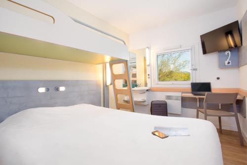 una camera d'albergo con letto bianco e scrivania di Ibis Budget Fréjus Capitou a Fréjus