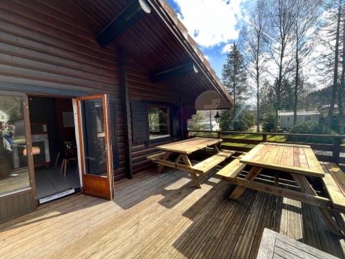 une terrasse en bois avec deux tables de pique-nique. dans l'établissement Chalet les Bleuets 12p - babyfoot & Wii, à Gérardmer