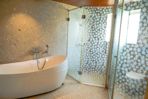 a bathroom with a tub and a glass shower at White Pearl Suites by Rosetum in Old Goa