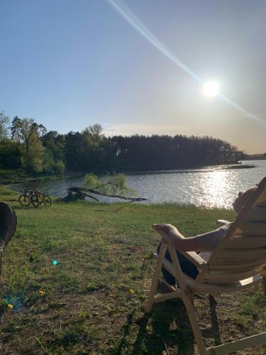 a person sitting in a chair next to a lake at Noclegi Little Sheep in Chojna