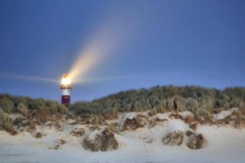 a light house on a beach with a rainbow at Ballumerhoeve Tree Lodge in Ballum