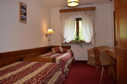 Cette chambre comprend deux lits, un bureau et une fenêtre. dans l'établissement HOTEL BOSCO VERDE, à Val di Zoldo