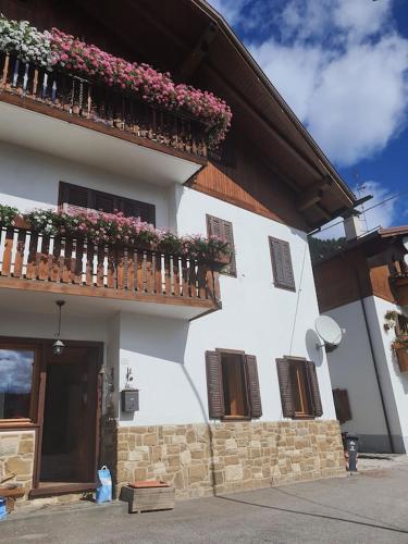 a white building with a balcony with flowers on it at Casa Phoenix Appartamento piano terra immerso nel verde a pochi minuti dalla ciclabile in Pieve di Cadore