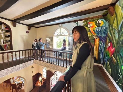 a woman standing in front of a painting of parrots at Hotel Boutique Spa Villa de Sant in Quito