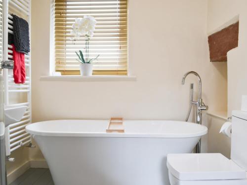 baño con bañera blanca y ventana en The Coach House, en Blencogo