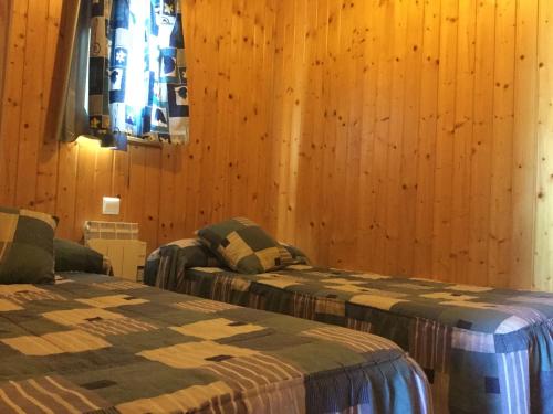two beds in a room with wooden walls at Casitas Cinco Castaños in Candelario